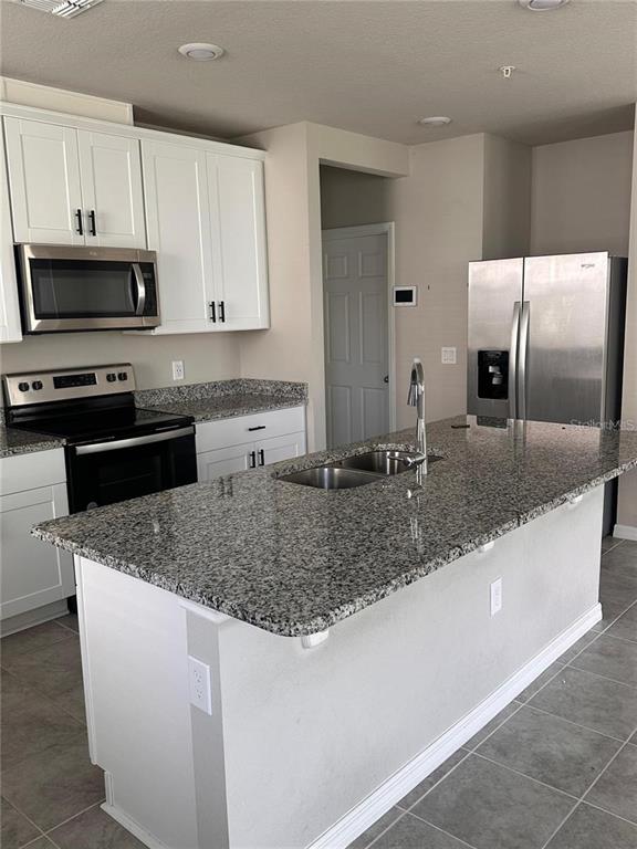 A kitchen features white cabinets, stainless steel appliances, and a granite-topped island with a sink — 2040 MILKWEED STREET, OCOEE, FL