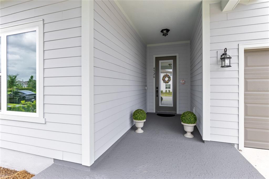 A covered entryway features light gray horizontal siding, a glass-paneled front door, and two planters — 6526 CIRCLE ROCK WAY, ST CLOUD, FL