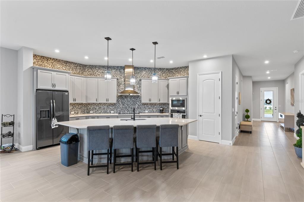 A modern kitchen features light gray cabinetry, a large island with seating, and tiled backsplash — 6526 CIRCLE ROCK WAY, ST CLOUD, FL