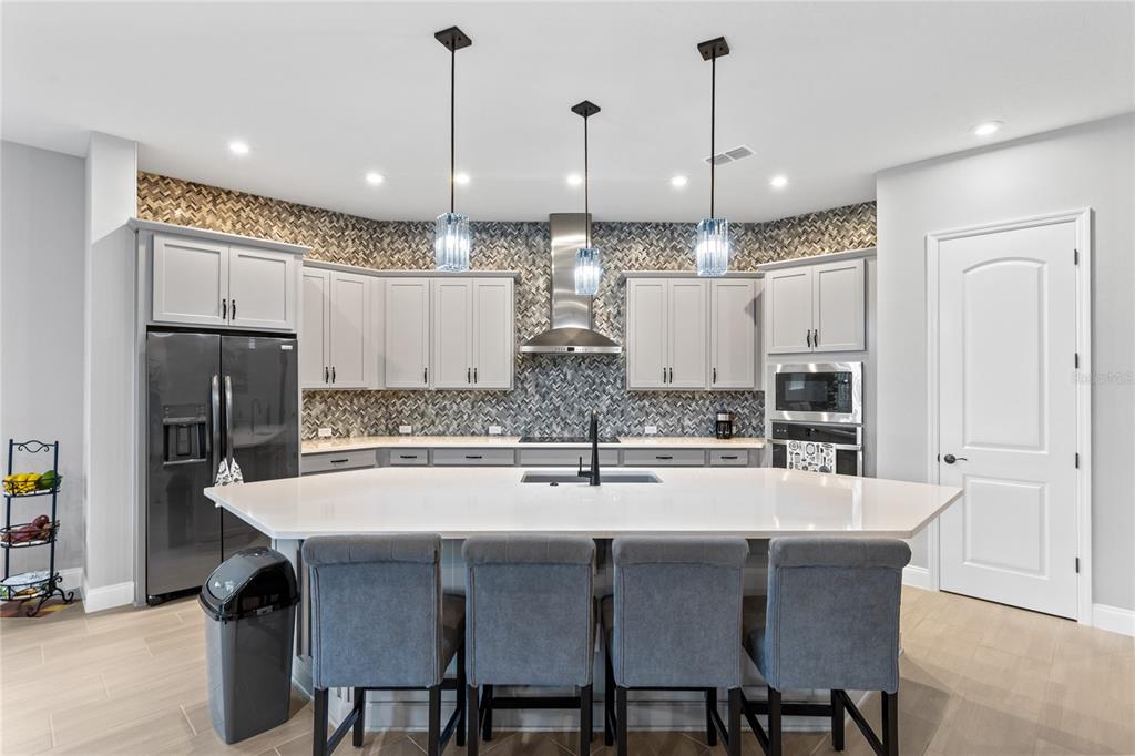 A modern kitchen features light gray cabinets, a large white island, and a herringbone backsplash — 6526 CIRCLE ROCK WAY, ST CLOUD, FL
