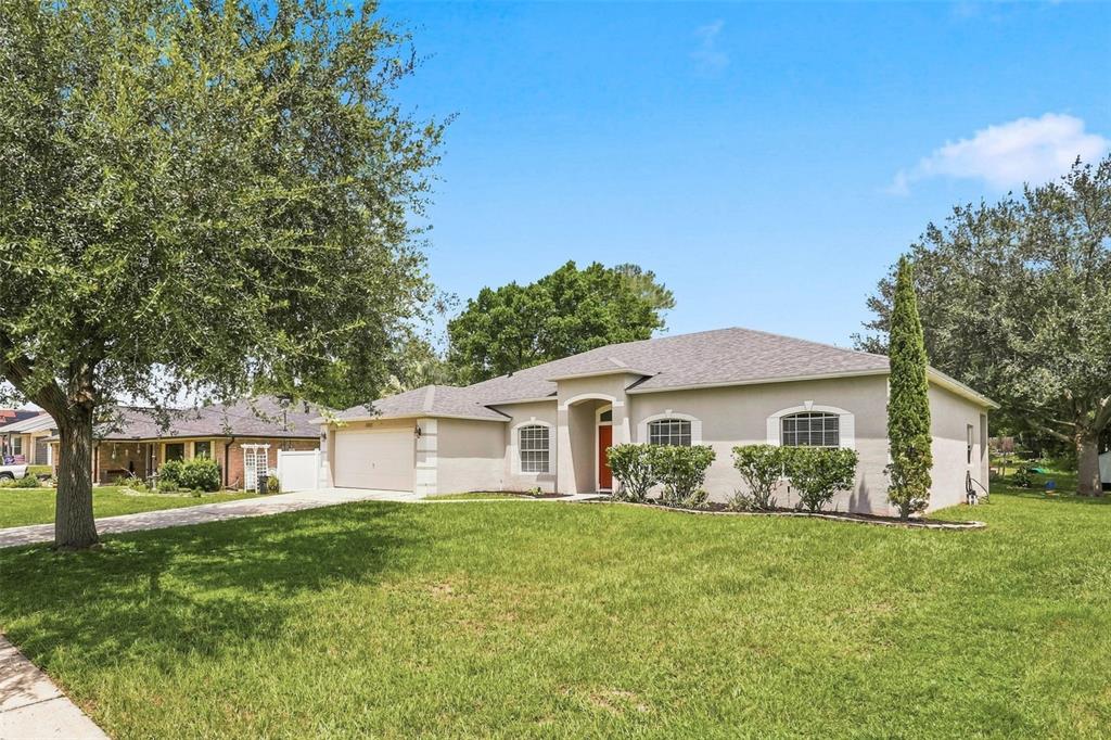 A single-story suburban house with a beige stucco exterior, a two-car garage, and a lawn — 1955 LINDHURST AVENUE, DELTONA, FL