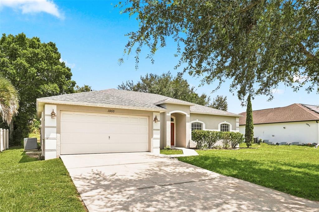 A single-story house with a two-car garage, beige stucco exterior, and a concrete driveway — 1955 LINDHURST AVENUE, DELTONA, FL