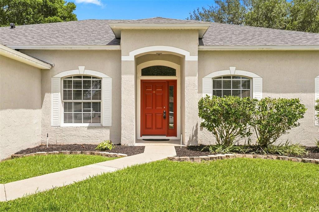 A single-story house with a red front door, arched windows, and a concrete walkway — 1955 LINDHURST AVENUE, DELTONA, FL