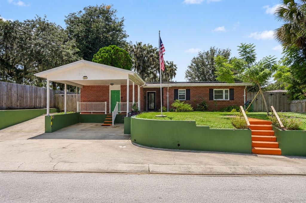 A single-story brick house features a covered carport, a green retaining wall, and orange steps — 2625 GARDEN STREET, TITUSVILLE, FL