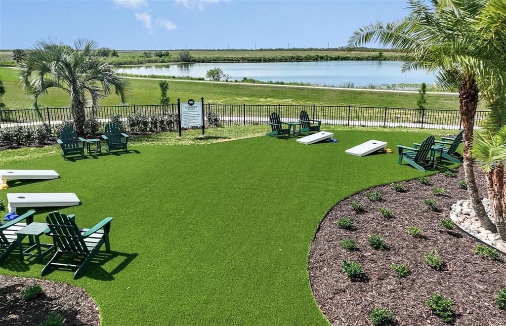 An outdoor recreational area features artificial turf, cornhole boards, green chairs, and a lake view — 465 WATERFORD DRIVE, LAKE ALFRED, FL