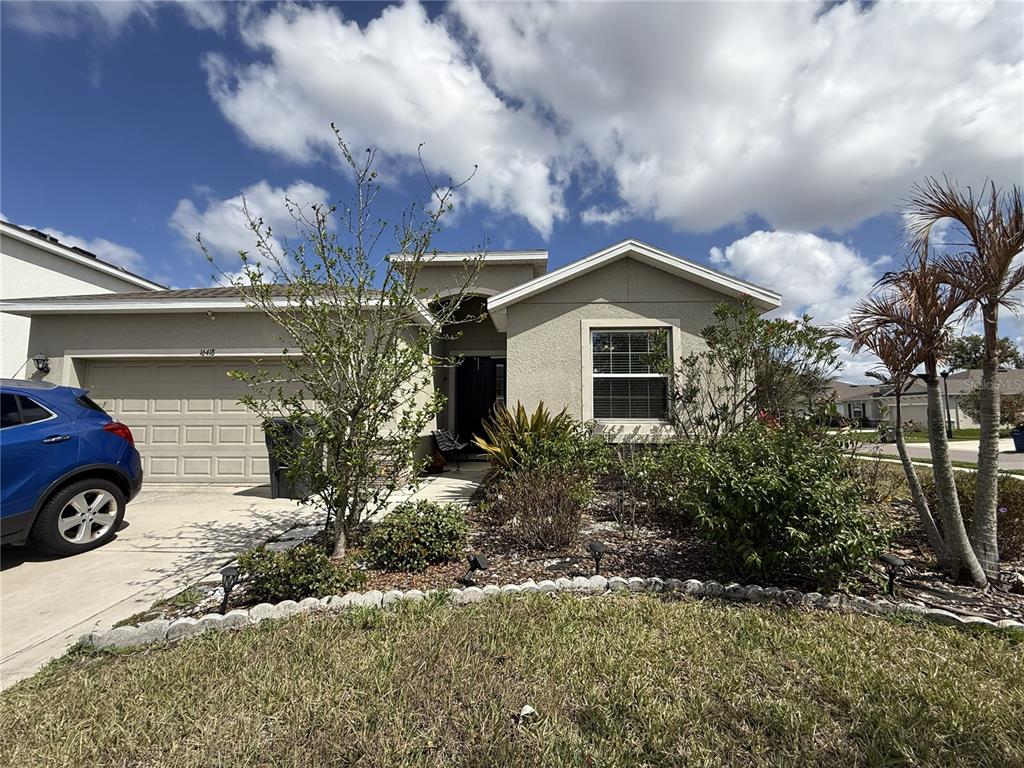 A single-story house with a beige stucco exterior, a two-car garage, and a landscaped yard — 16418 WOODSIDE GLEN, PARRISH, FL