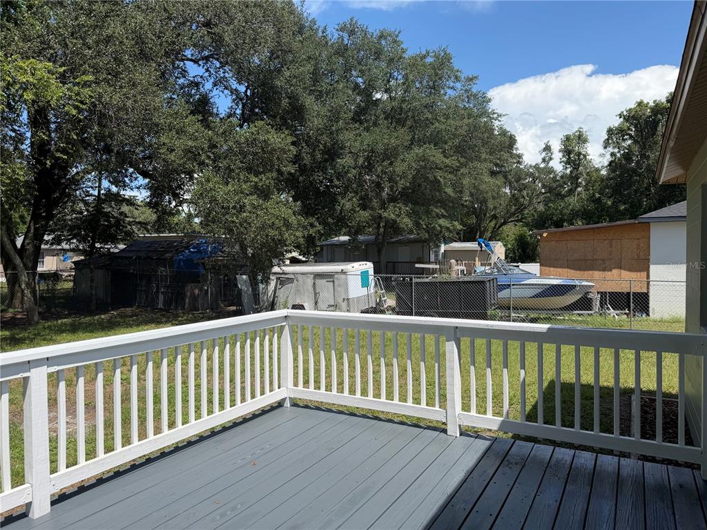 A gray wooden deck with a white railing overlooks a backyard with a boat and trailer — 21015 MARKET STREET, DADE CITY, FL