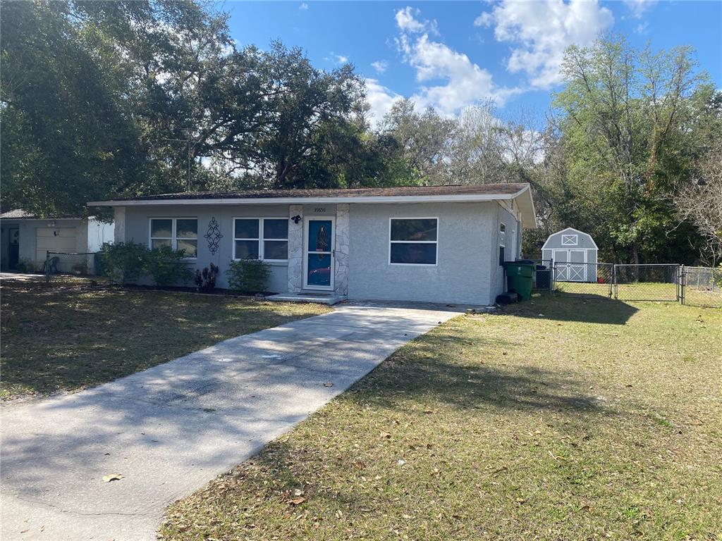 A single-story gray house with a concrete driveway, a front door, and a backyard shed — 39656 MEADOWOOD LOOP, ZEPHYRHILLS, FL