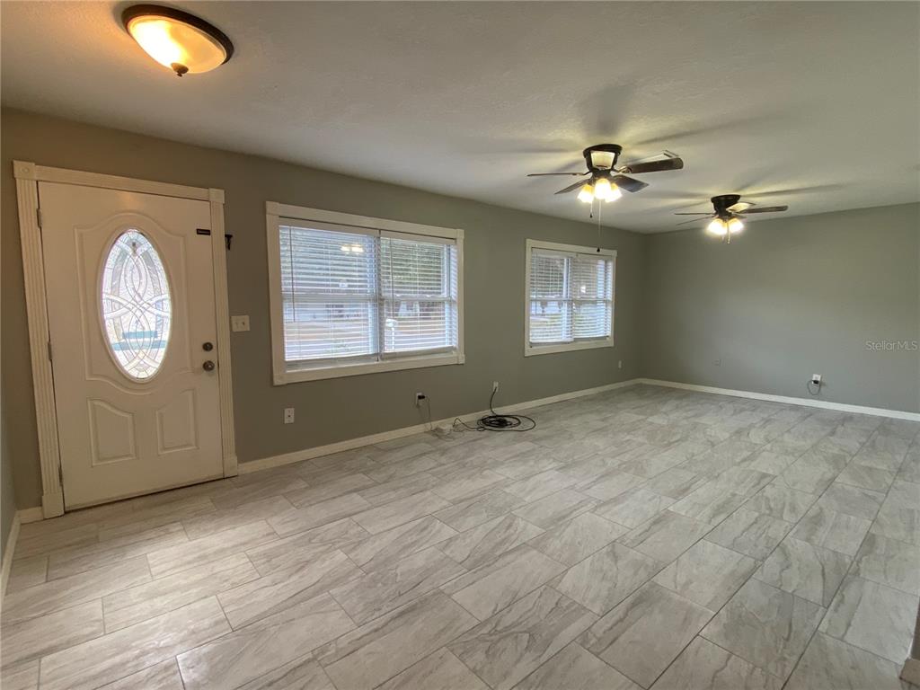 A living room features light gray walls, wood-look tile flooring, two ceiling fans, and a door — 39656 MEADOWOOD LOOP, ZEPHYRHILLS, FL