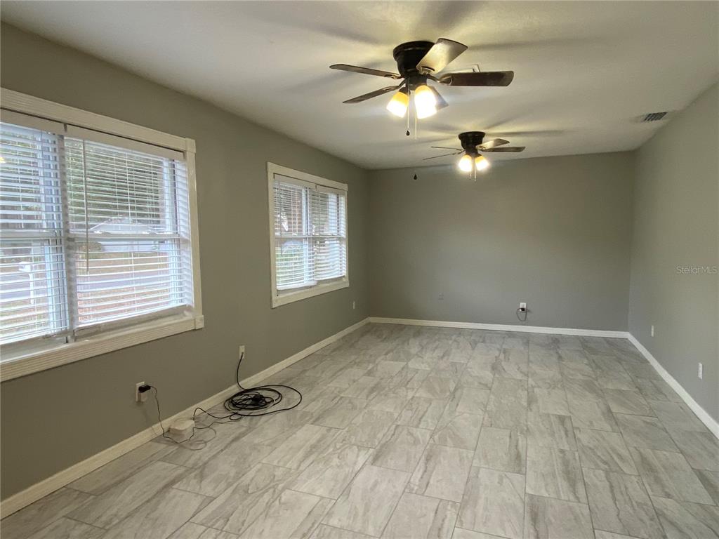 An empty room features gray walls, light-colored tile flooring, two windows, and two ceiling fans — 39656 MEADOWOOD LOOP, ZEPHYRHILLS, FL
