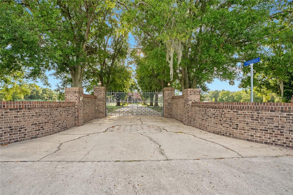 A brick wall and iron gate lead to a tree-lined driveway at a gated entrance — 4410 ALBRITTON ROAD, ST CLOUD, FL