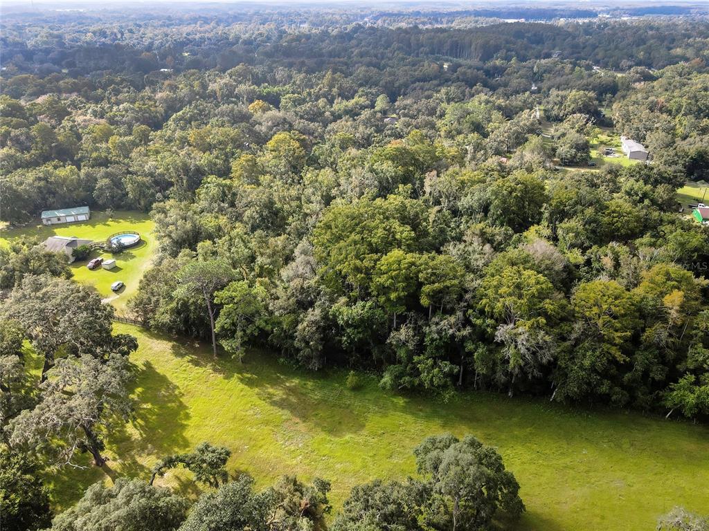 An aerial view shows a grassy field, a wooded area, and a house with a pool — 0 PALMER LANE, SPRING HILL, FL