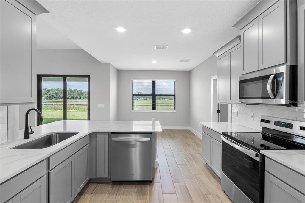 A modern kitchen features gray cabinets, white countertops, stainless steel appliances, and wood-look tile flooring — 13501 WALDEN SHEFFIELD ROAD, DOVER, FL