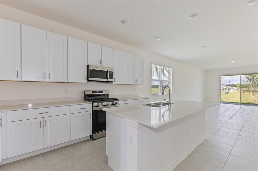 A kitchen features white cabinets, stainless steel appliances, a center island, and tile flooring — 9128 WILDLIGHT TRAIL, WILDWOOD, FL