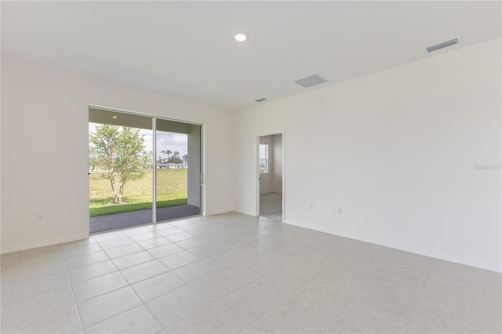 A bright, empty room features light-colored tile flooring, white walls, and sliding glass patio doors — 9128 WILDLIGHT TRAIL, WILDWOOD, FL