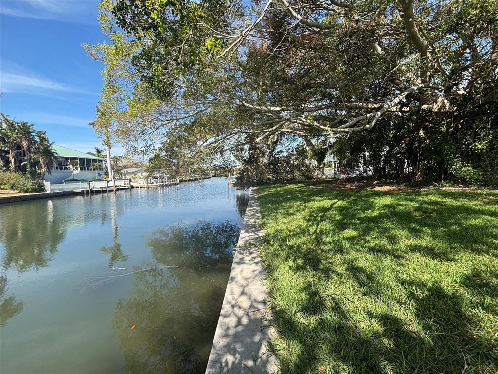 A grassy waterfront lot features a concrete seawall bordering a canal with trees overhead — 4417 DOLPHIN LANE, PALMETTO, FL