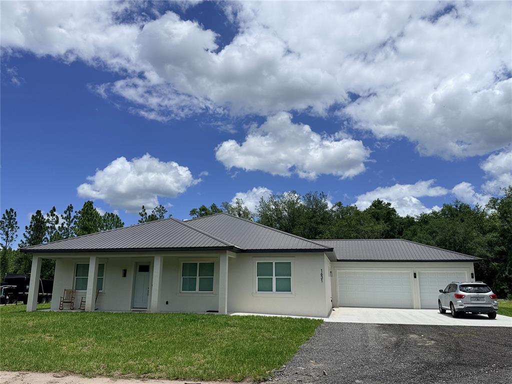A single-story house with a metal roof, white stucco exterior, and an attached three-car garage — 2410 LAKE TINY ROAD, DELTONA, FL