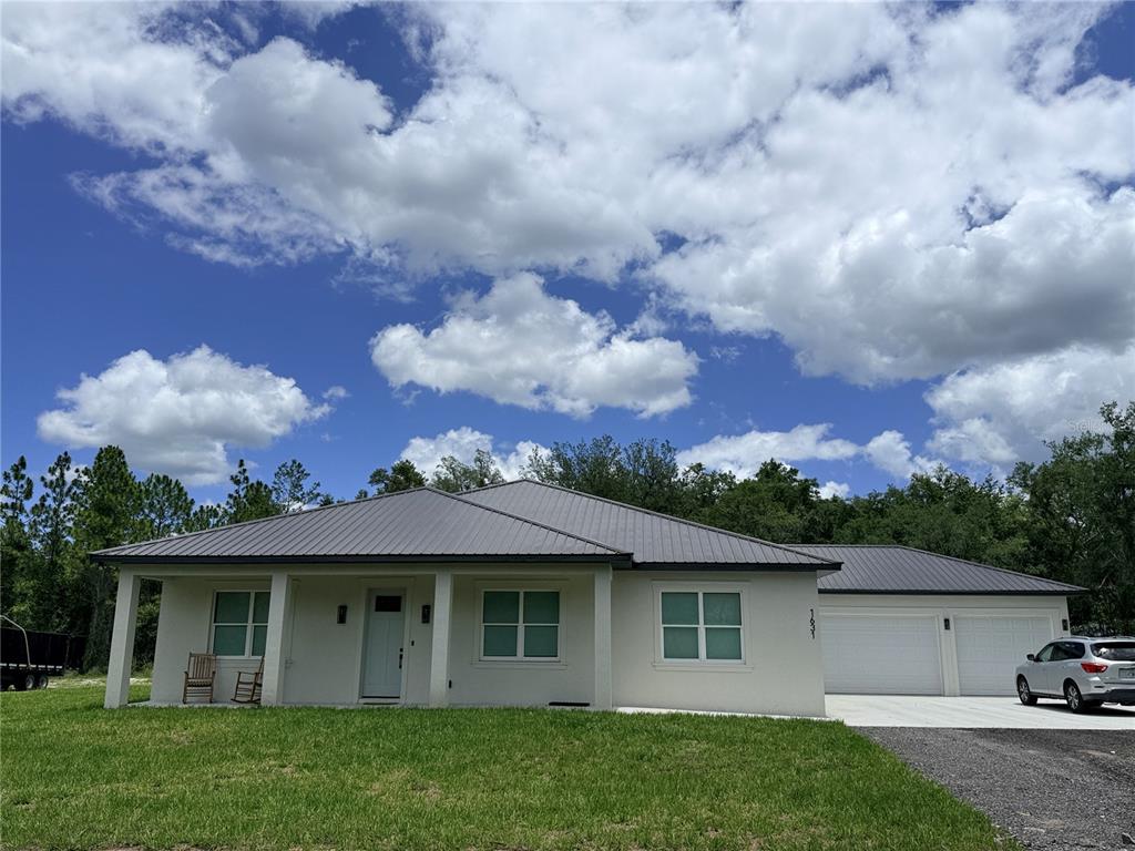 A single-story house with a metal roof, white stucco exterior, and an attached two-car garage — 2410 LAKE TINY ROAD, DELTONA, FL