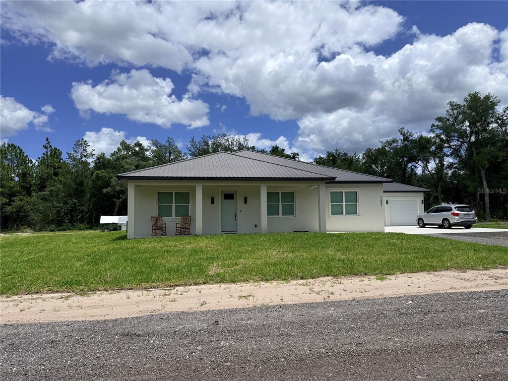 A single-story house with a metal roof, light-colored stucco exterior, and an attached garage — 2410 LAKE TINY ROAD, DELTONA, FL