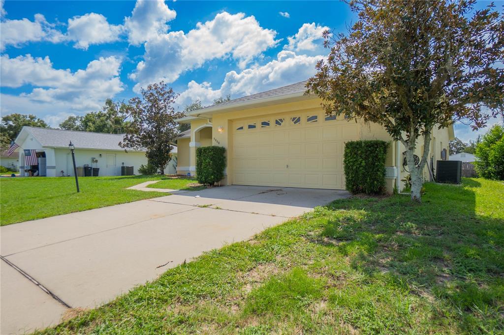 A yellow house with a two-car garage and a concrete driveway under a blue sky — 3200 S FRANKLIN TERRACE, INVERNESS, FL