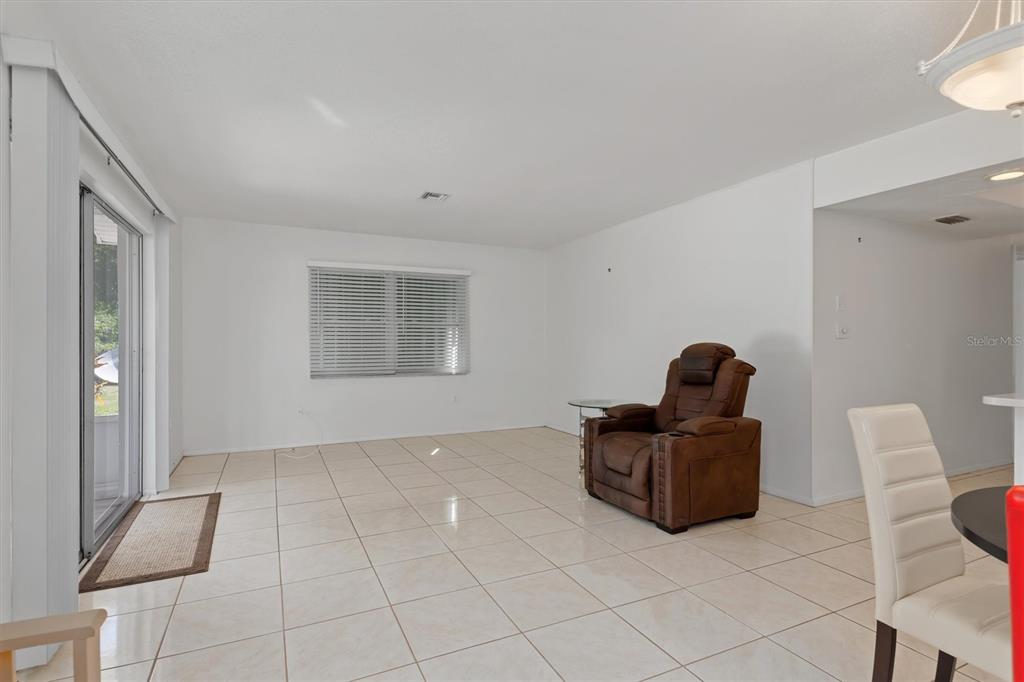 A living room with white walls, light tile flooring, a sliding glass door, and a recliner — 8126 RIVERSIDE DRIVE, PUNTA GORDA, FL