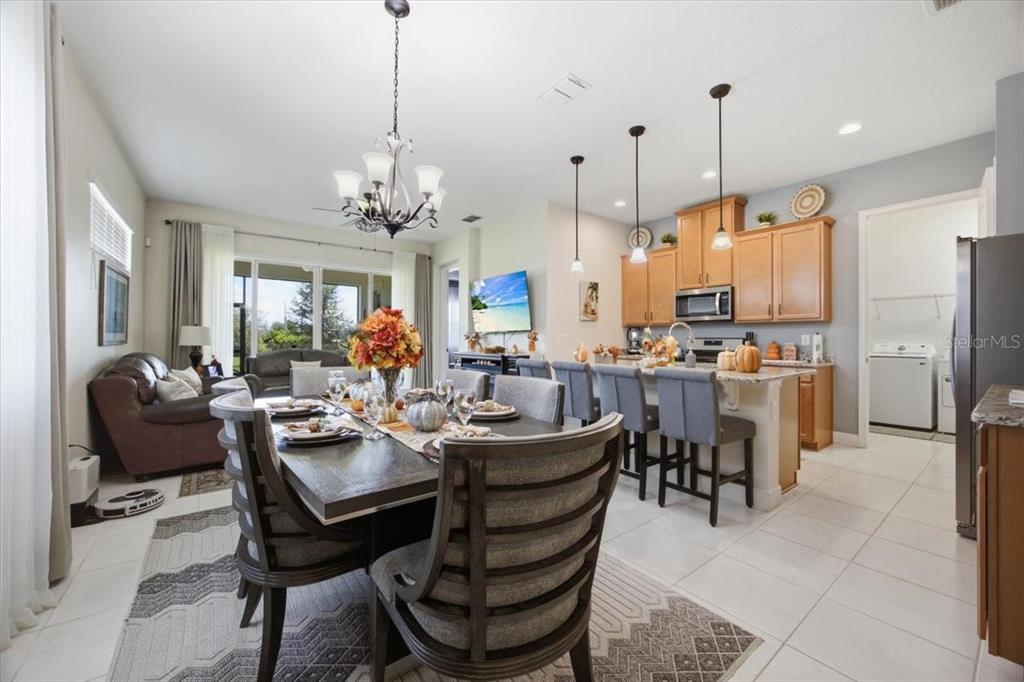 An open-concept dining area and kitchen feature light wood cabinets, tile flooring, and a chandelier — 2541 YELLOW BRICK ROAD, ST CLOUD, FL