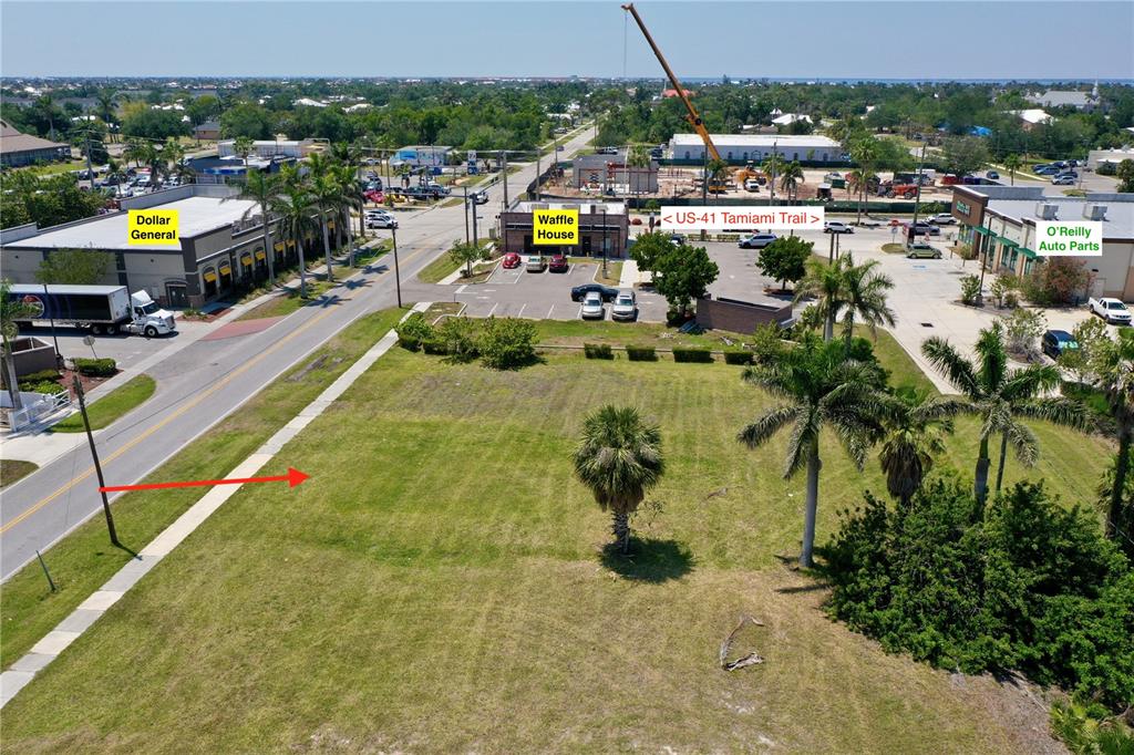 An aerial view shows a vacant grassy lot adjacent to a road and commercial buildings — 122 E MCKENZIE STREET, PUNTA GORDA, FL