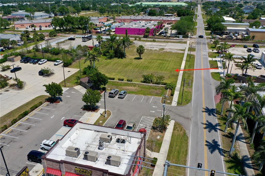 An aerial view shows a vacant grassy lot adjacent to a Waffle House and road — 122 E MCKENZIE STREET, PUNTA GORDA, FL