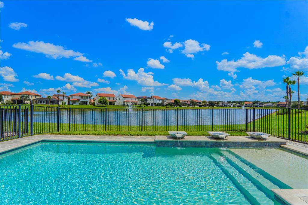 A swimming pool with water features overlooks a lake and a residential neighborhood under blue skies — 10427 ROYAL CYPRESS WAY, ORLANDO, FL