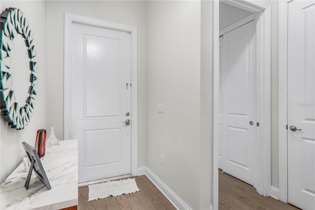 A bright entryway features a white door, a round decorative mirror, and light wood flooring — 10427 ROYAL CYPRESS WAY, ORLANDO, FL