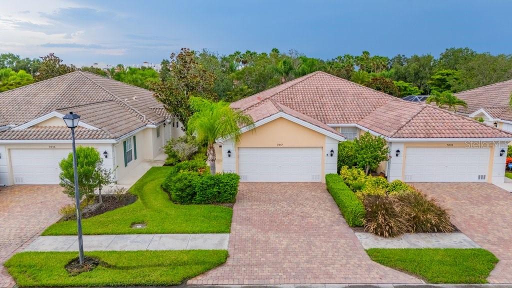 An exterior view of three attached single-story houses with tiled roofs and brick paver driveways — 7617 CAMMINARE DRIVE, SARASOTA, FL