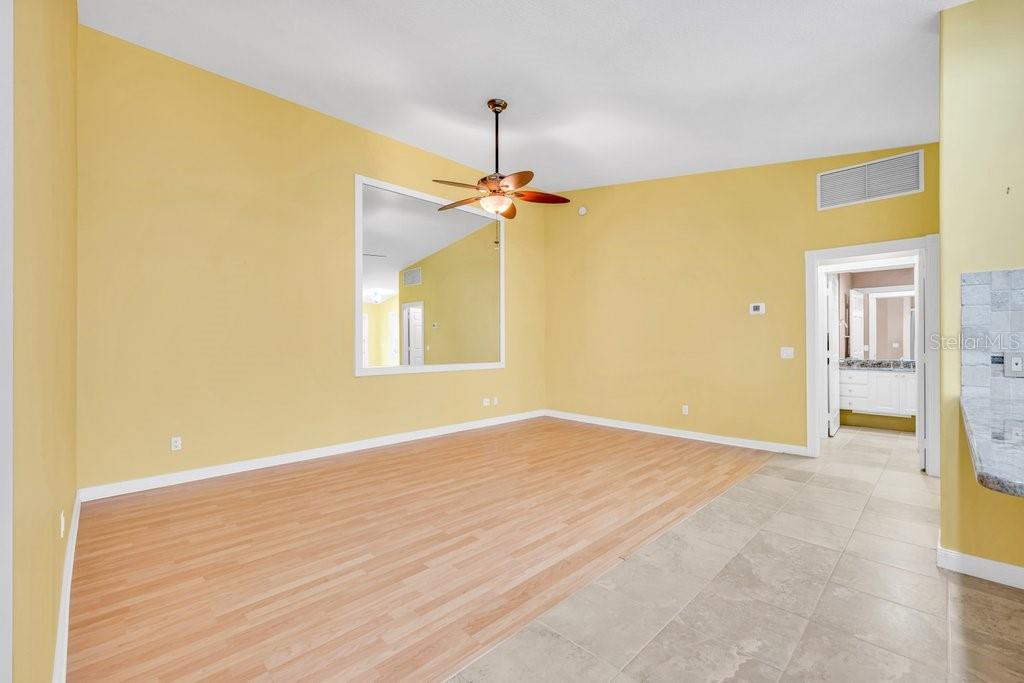 An empty room with yellow walls, light wood-look flooring, a ceiling fan, and a mirror — 7617 CAMMINARE DRIVE, SARASOTA, FL