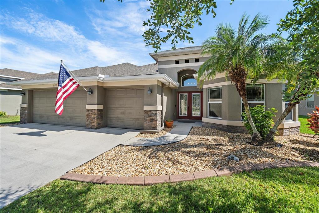 A single-story house with a two-car garage, stone accents, and a palm tree in front — 11220 77TH STREET E, PARRISH, FL