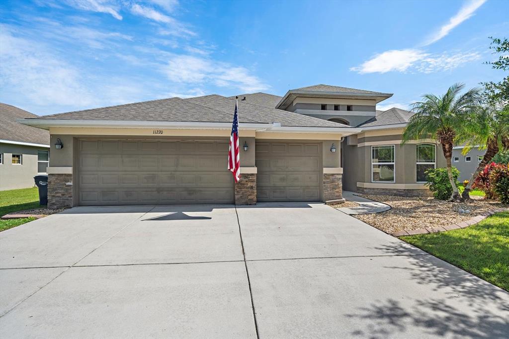 A single-story house with a three-car garage, stone accents, and an American flag — 11220 77TH STREET E, PARRISH, FL