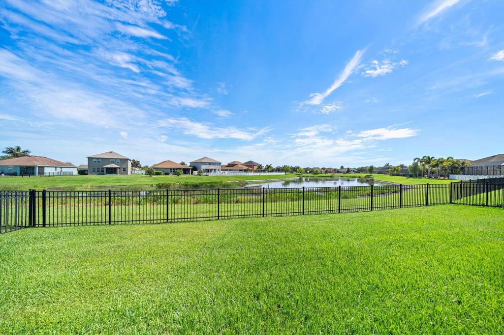 A grassy backyard features a black metal fence overlooking a pond and suburban houses — 11220 77TH STREET E, PARRISH, FL
