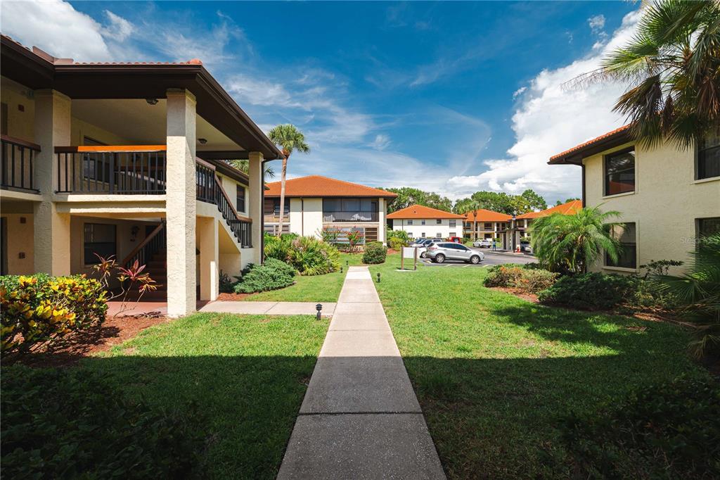 A concrete walkway leads between two-story apartment buildings with balconies and red tile roofs — 1109 HAMMOCK PINE BOULEVARD, CLEARWATER, FL