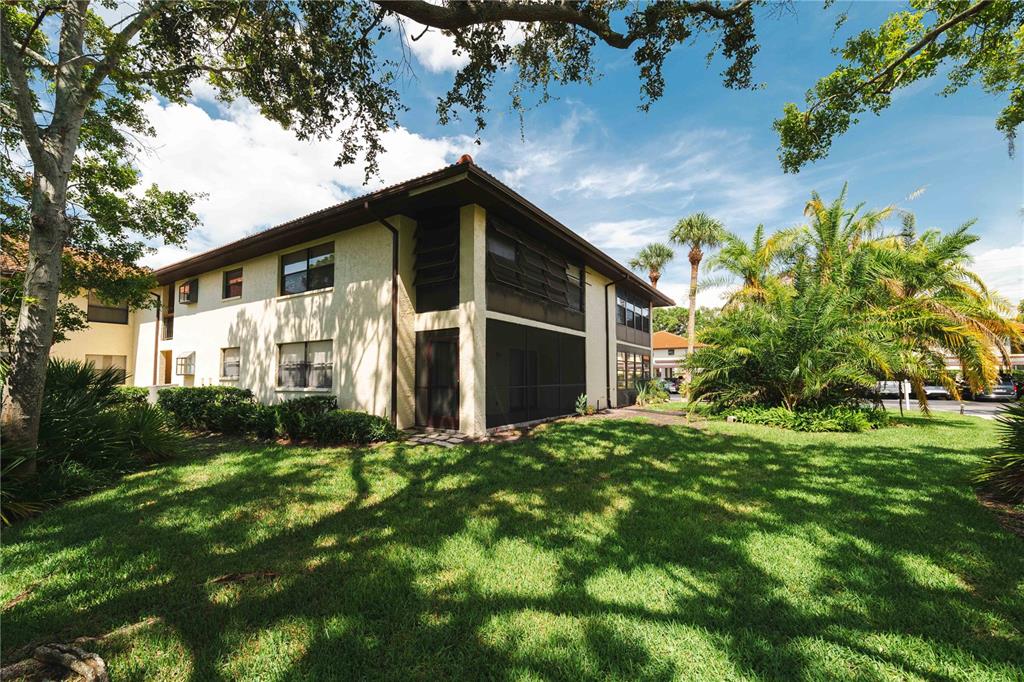 A two-story apartment building with a screened-in patio sits on a grassy lawn with trees — 1109 HAMMOCK PINE BOULEVARD, CLEARWATER, FL