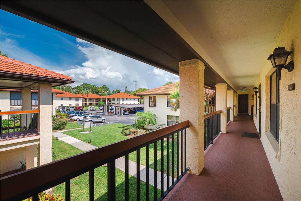 An outdoor covered walkway with railings overlooks a parking lot and apartment buildings — 1109 HAMMOCK PINE BOULEVARD, CLEARWATER, FL
