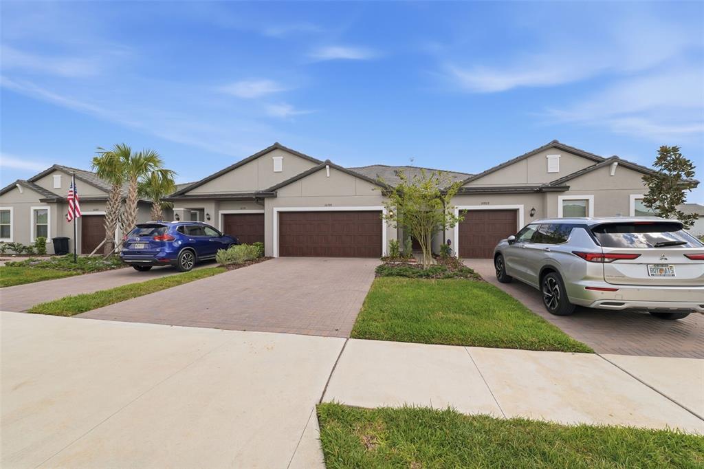 A row of single-story townhomes with attached garages and paved driveways under a blue sky — 10799 GABLE DIG LOOP, SAN ANTONIO, FL