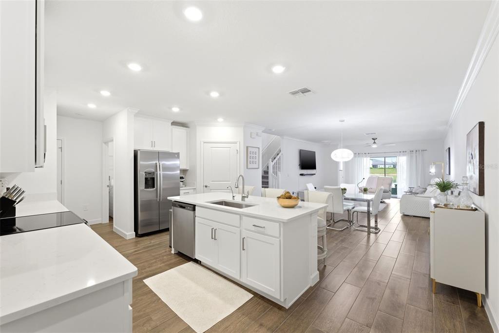 A bright, open-concept kitchen features white cabinetry, a central island, and wood-look tile flooring — 10799 GABLE DIG LOOP, SAN ANTONIO, FL