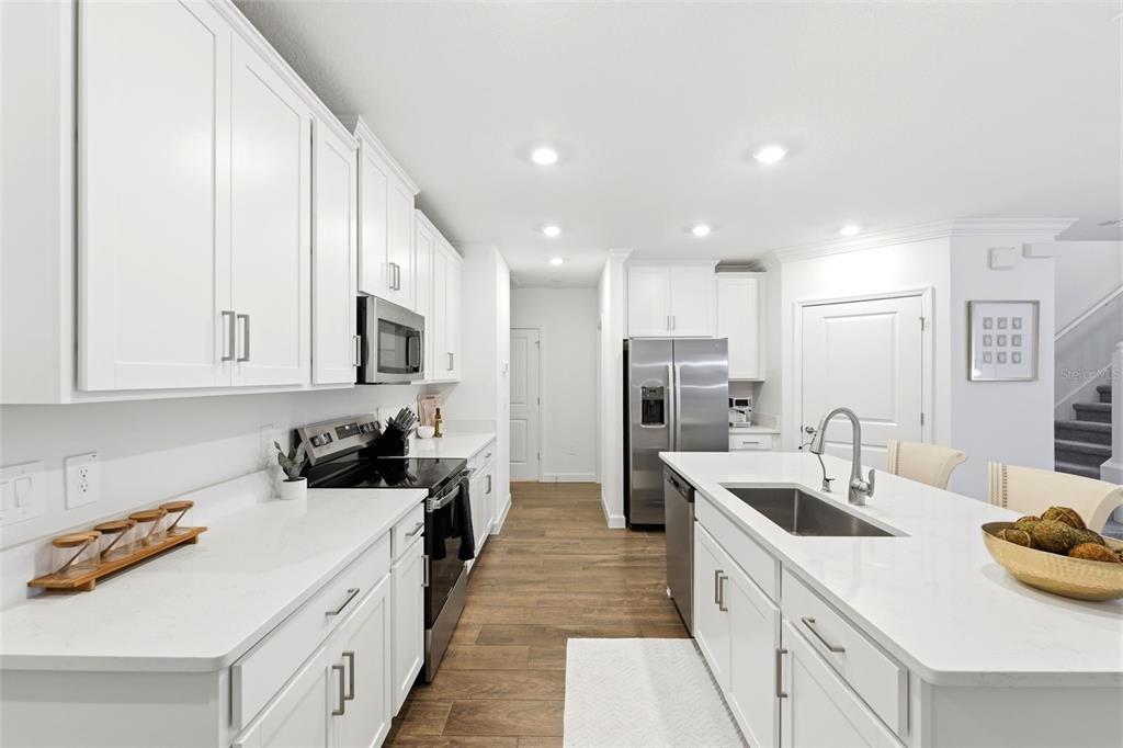A modern kitchen features white cabinets, quartz countertops, stainless steel appliances, and wood-look flooring — 10799 GABLE DIG LOOP, SAN ANTONIO, FL