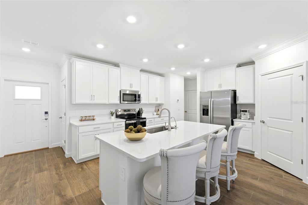 A modern kitchen features white cabinetry, stainless steel appliances, a quartz island, and wood-look flooring — 10799 GABLE DIG LOOP, SAN ANTONIO, FL