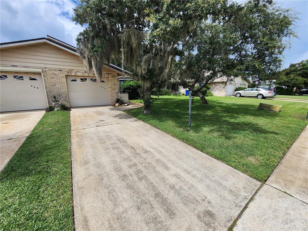 A concrete driveway leads to a one-story house with a two-car garage and large trees — 322 PARADISE LANE, EDGEWATER, FL