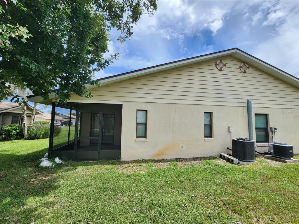 The exterior of a house features a screened-in porch, beige siding, and two HVAC units — 322 PARADISE LANE, EDGEWATER, FL