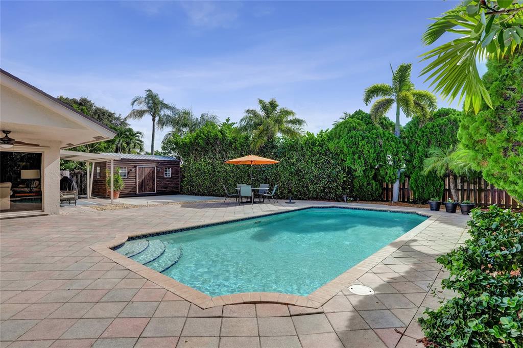A backyard features a swimming pool, a paved patio, an orange umbrella, and a wooden shed — 1156 SW 149 LANE, SUNRISE, FL
