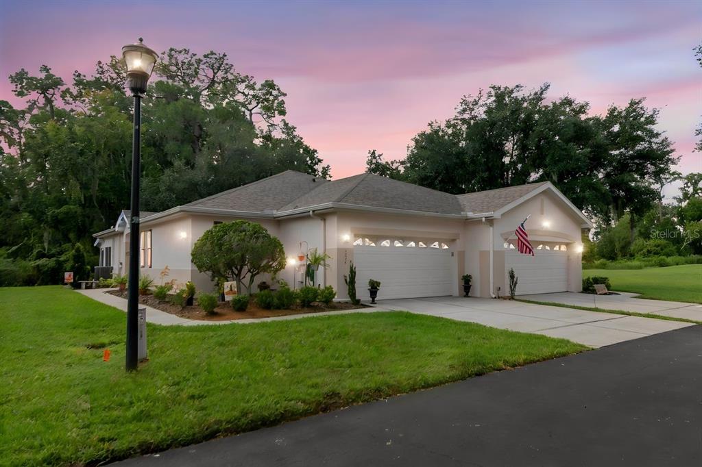 A single-story house with a three-car garage and an American flag at dusk — 2635 EAGLE GREENS DRIVE, PLANT CITY, FL