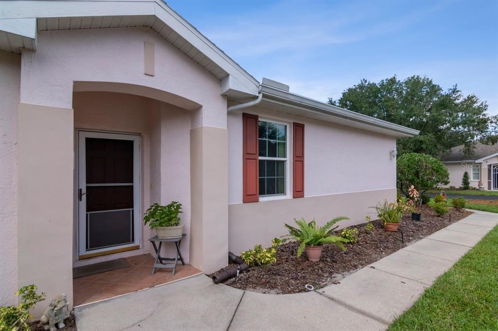 A light pink house exterior features a front entrance, a window with red shutters, and landscaping — 2635 EAGLE GREENS DRIVE, PLANT CITY, FL