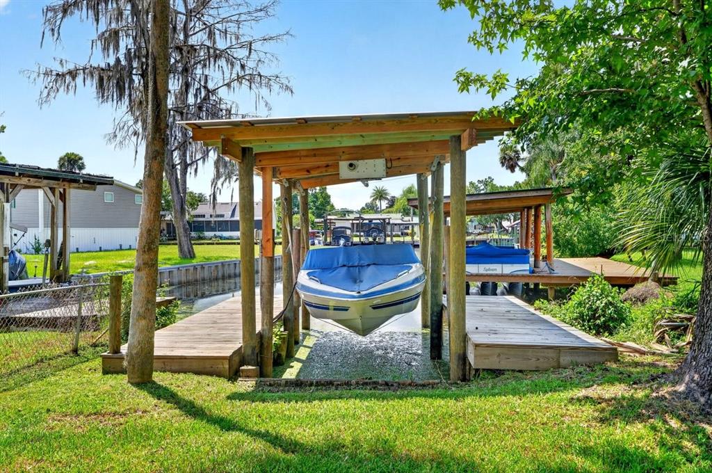 A boat sits on a lift under a wooden canopy beside a grassy waterfront yard — 55707 JAMIE DRIVE, ASTOR, FL