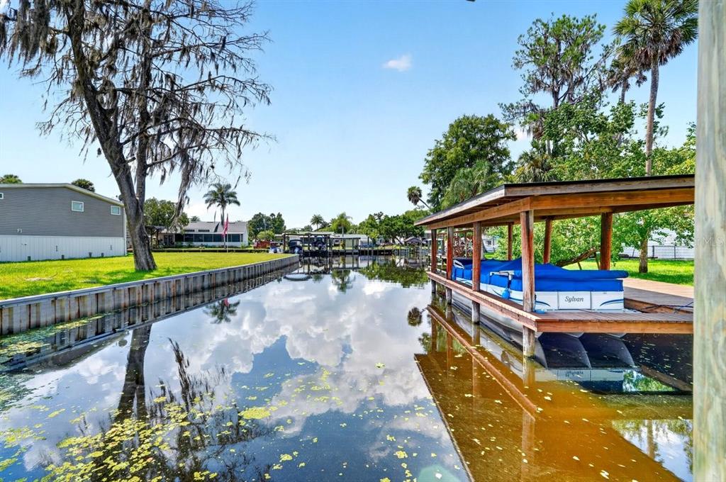 A boat docked in a canal next to a grassy yard with a large tree — 55707 JAMIE DRIVE, ASTOR, FL
