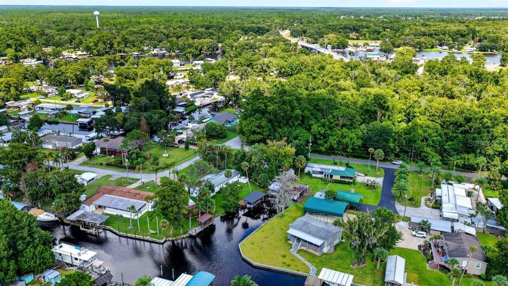 An aerial view shows houses situated along a canal surrounded by dense green trees — 55707 JAMIE DRIVE, ASTOR, FL